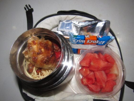 Nigerian school lunchbox meal of spaghetti with stew served with a side of watermelon