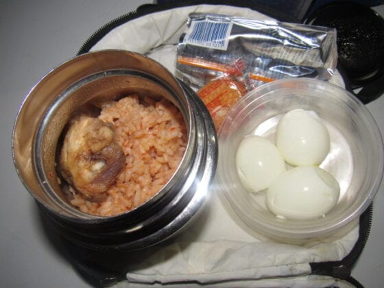 Nigerian school lunchbox meal of jollof rice with chicken and a side of boiled eggs