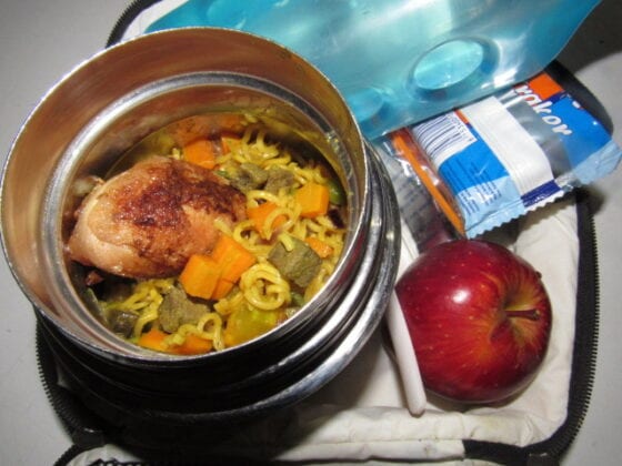 Nigerian school lunchbox meal of fried noodles with chicken served with a side of apple